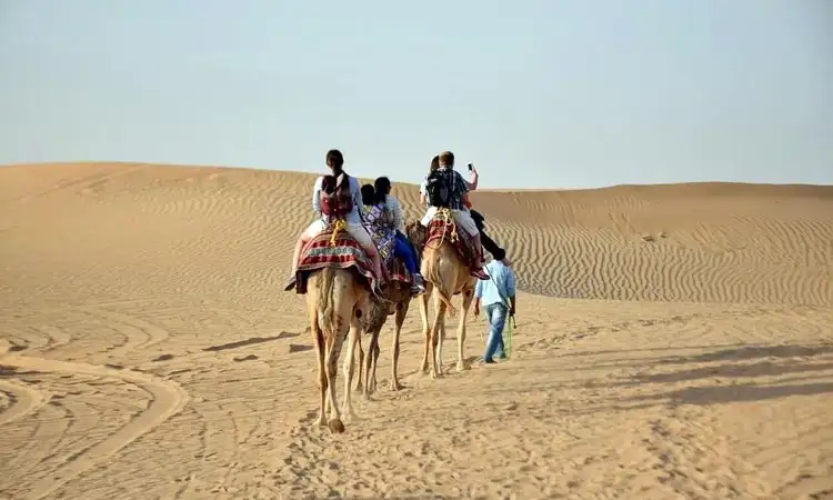 A serene morning scene in the Abu Dhabi desert with 4x4 vehicles, camel rides, and golden sand dunes under the soft glow of the early morning sun.