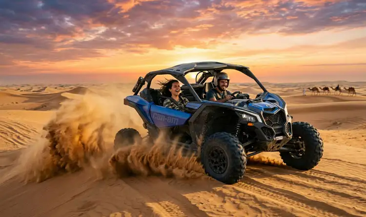 A smiling man and woman driving a blue Can-Am off-road buggy, kicking up sand on a dune in Abu Dhabi with a camel caravan in the distant background.