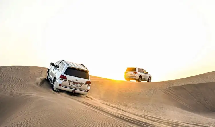 White SUVs dune bashing in desert at sunset, sand flying, golden light.