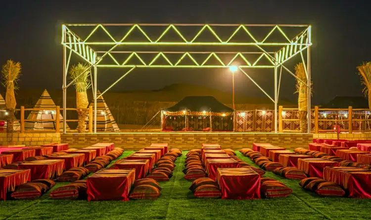 Neon-green lit stage and traditional red cushion seating in a desert camp at night, Arabian luxury outdoor venue.