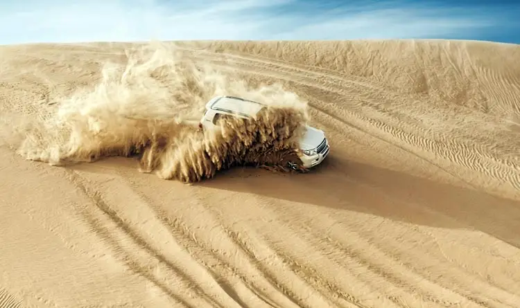 White 4x4 Land Cruiser kicking up a cloud of sand while dune bashing during an evening desert safari in Abu Dhabi.