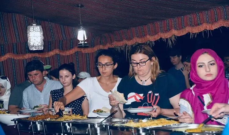 Tourists enjoying a buffet dinner inside a Bedouin-style tent during an evening desert safari in Abu Dhabi.
