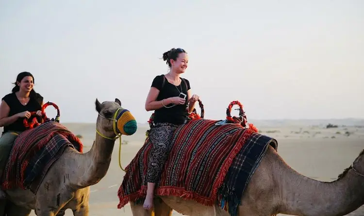 Women riding camels across the sand dunes during an evening desert tour in Abu Dhabi.