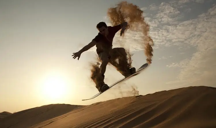 Sandboarder performing an athletic jump trick on sand dunes at sunset during an Abu Dhabi desert safari.
