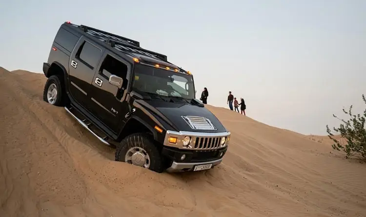 Black Hummer H2 navigating down a steep sand dune during an off-road safari in Abu Dhabi.