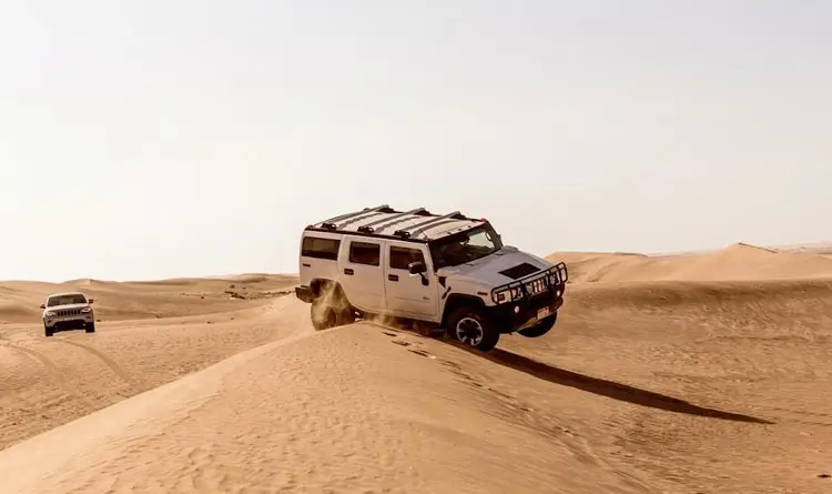 White Hummer SUV driving along the ridge of sand dunes during an Abu Dhabi desert tour.