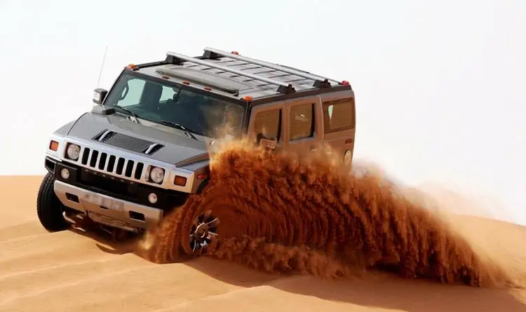 Hummer SUV kicking up a large spray of sand while dune bashing in the Abu Dhabi desert.