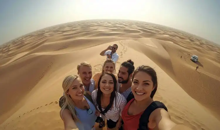 A group of travelers on a dune in the Abu Dhabi desert, posing for a photograph against a stunning backdrop of sand dunes and blue sky.