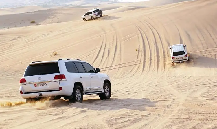 White 4x4 SUVs dune bashing across the golden sand dunes during a sunrise desert safari in Abu Dhabi.