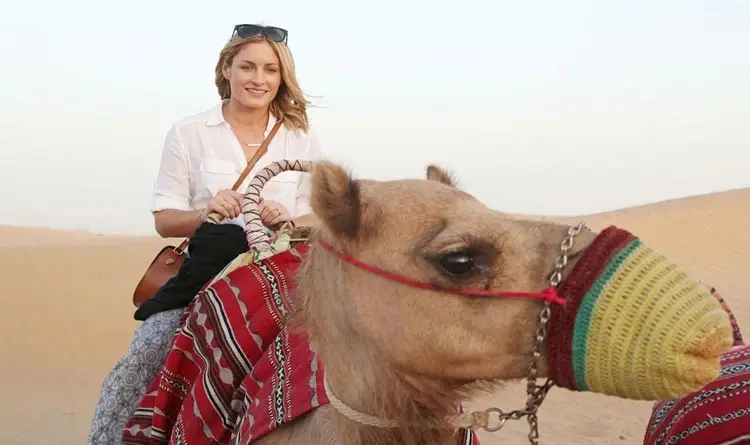 Smiling woman riding a decorated camel during a morning desert tour in Abu Dhabi.